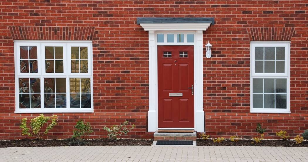 red composite entrance door on red brick house with white uPVC casement windows